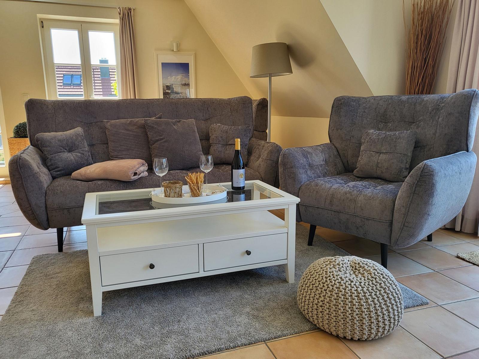 Wohnzimmer mit grauem Sofa, Sessel, weißem Couchtisch und Teppich.