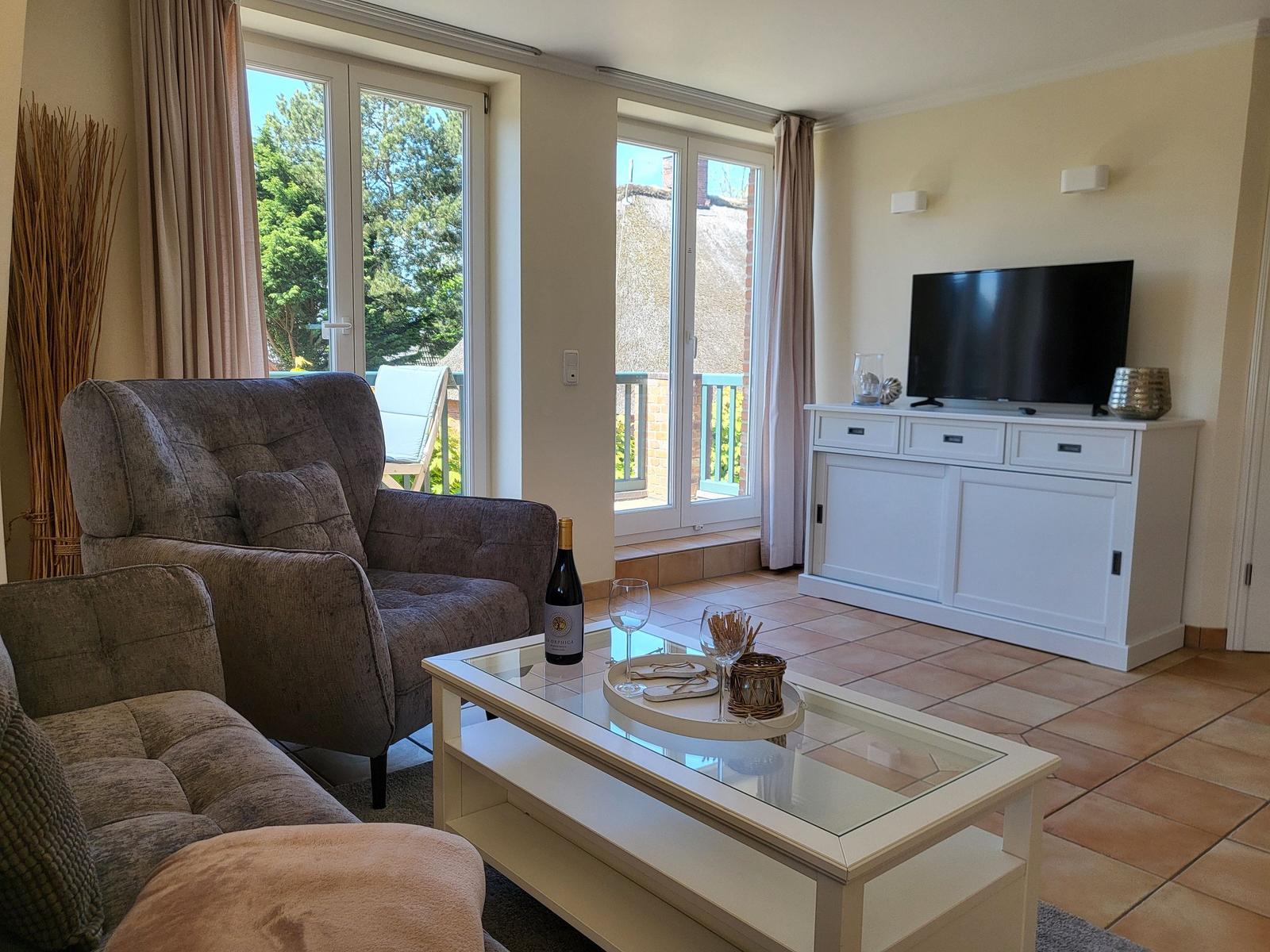 Wohnzimmer mit Sofa, Fernseher und Terrassentür. Auf Tisch steht Wein und Gläser.