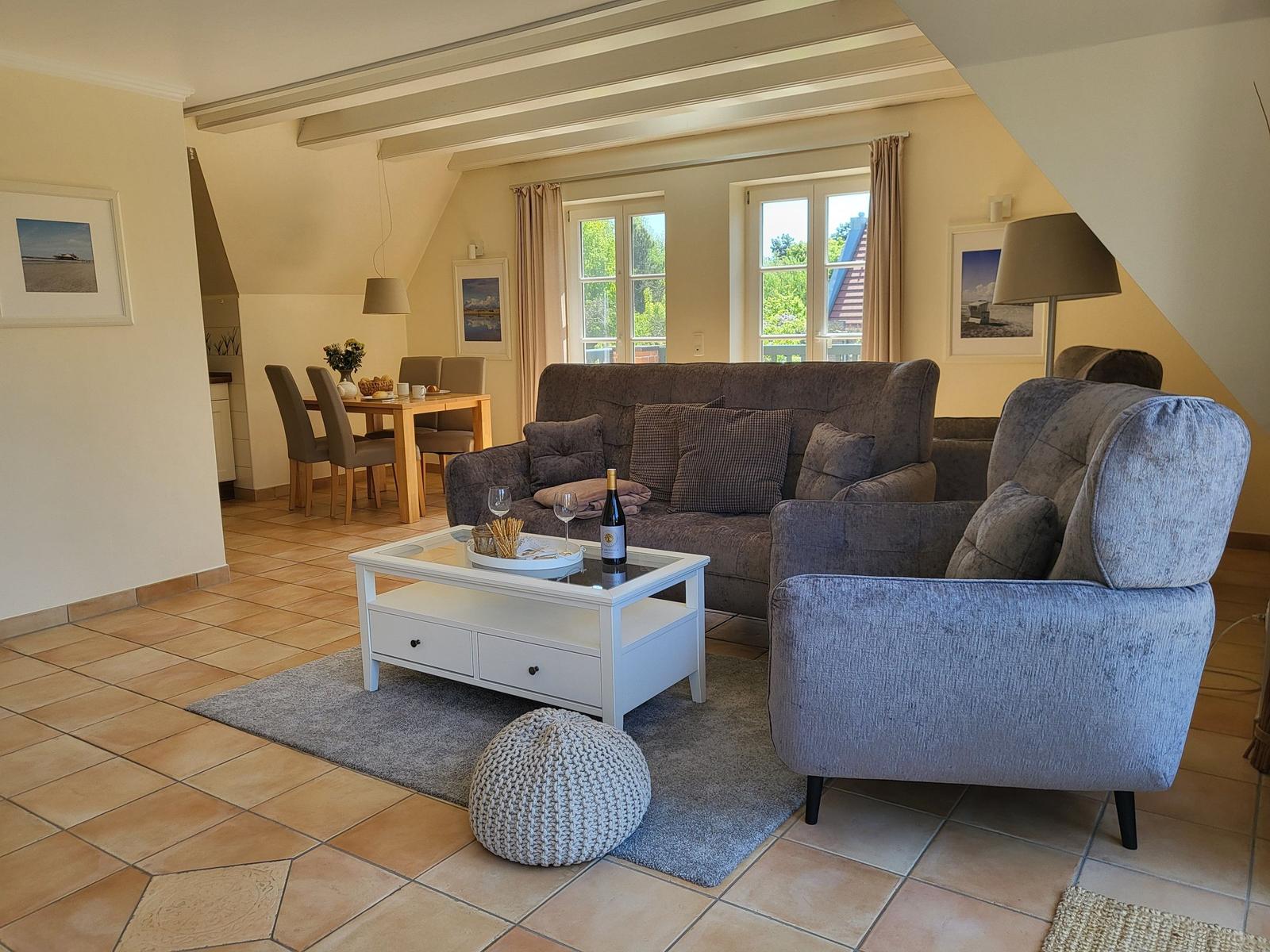 Wohn- und Essbereich mit Sofa, Sessel und Esstisch. Holzboden und Fenster.