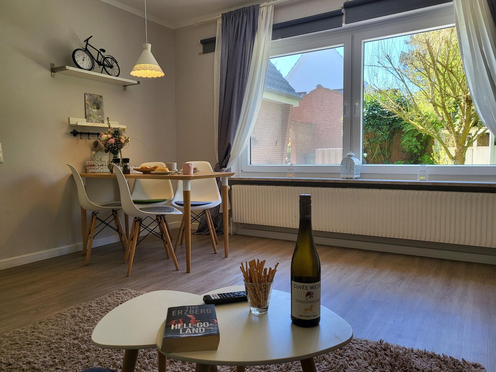 Essbereich mit Tisch, Stühlen und Blick auf Garten. Tisch mit Wein und Buch.