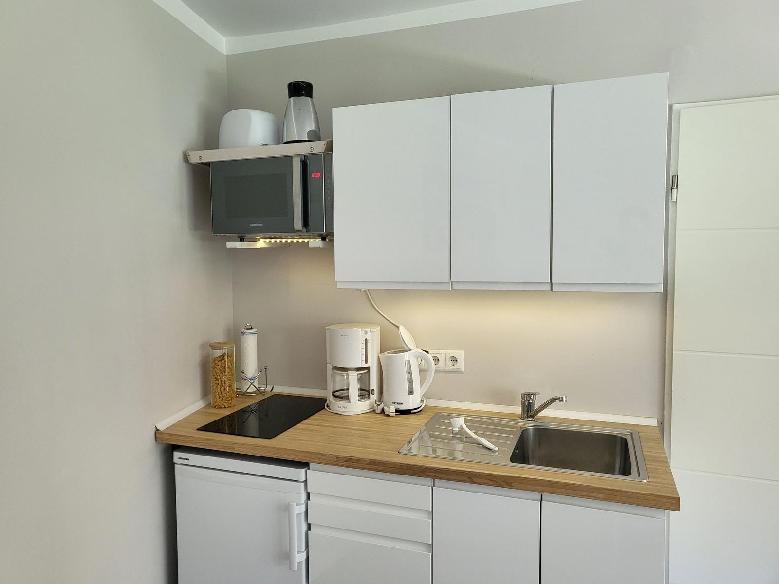 Küche mit Arbeitsplatte, Spüle, Kühlschrank und Mikrowelle.