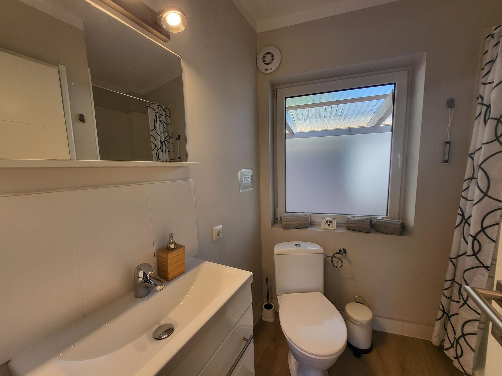 Badezimmer mit Waschbecken, Toilette und Fenster mit Tuch.
