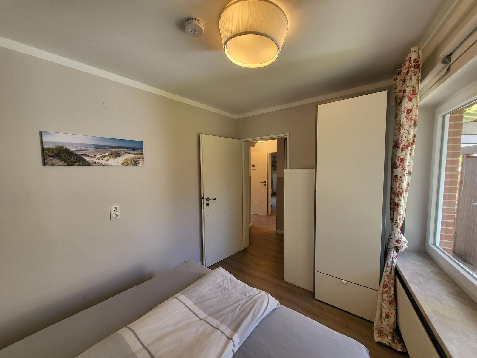 Schlafzimmer mit Bett, Kleiderschrank und Fenster mit Blumenvorhang.