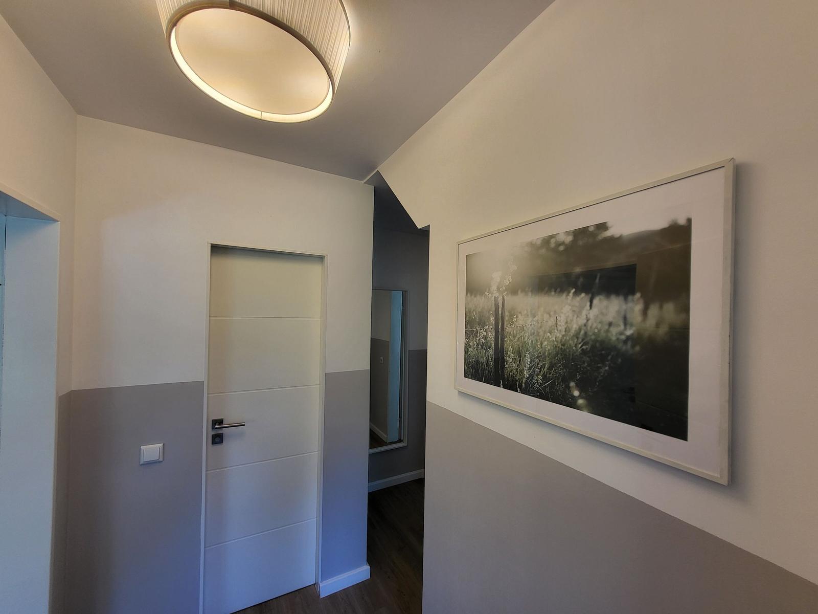 Flur mit Wandbild und Tür. Deckenleuchte und zweifarbige Wände.