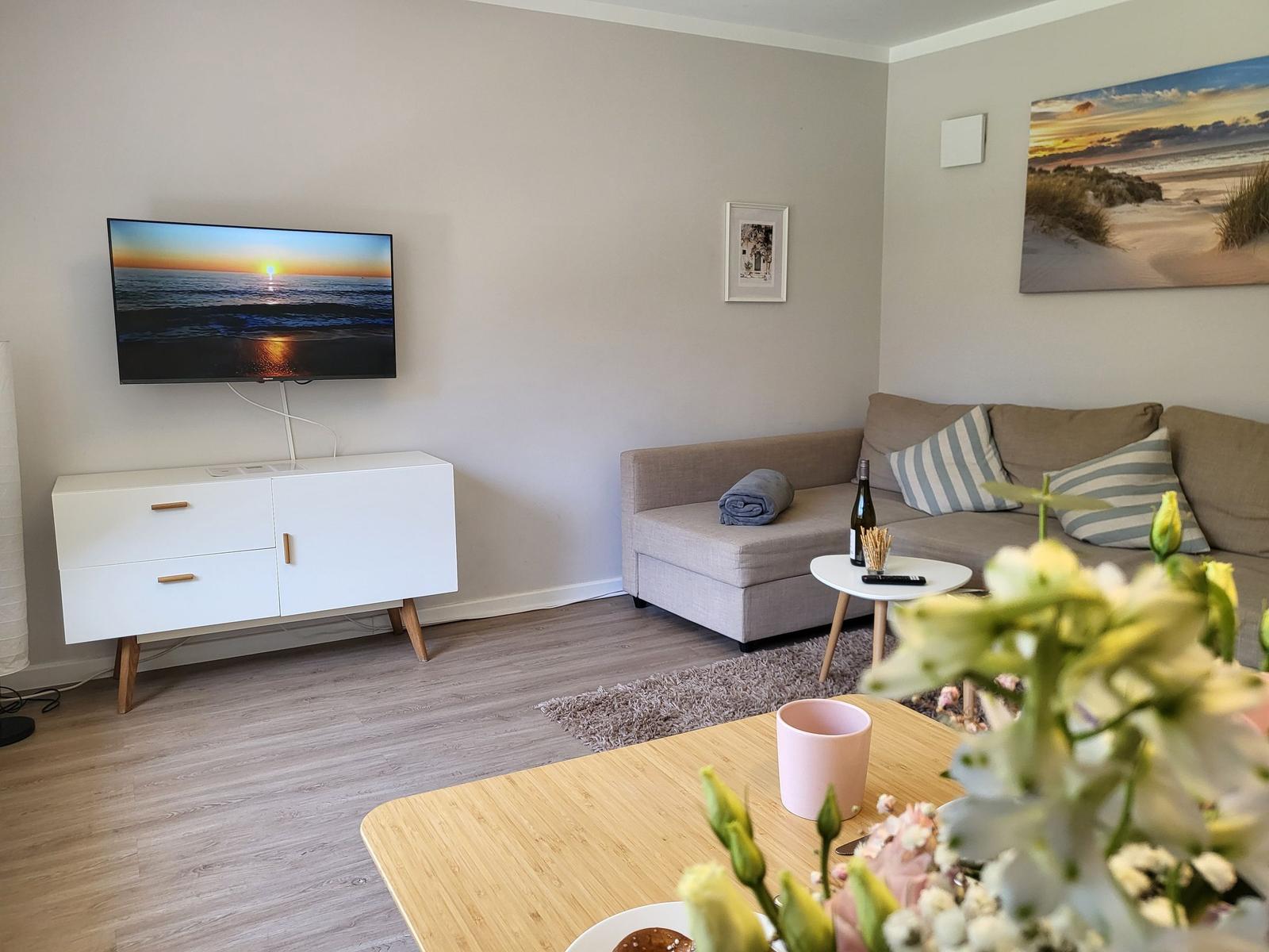 Wohnzimmer mit Sofa, Fernseher und Tisch. Wandbild zeigt Strand.