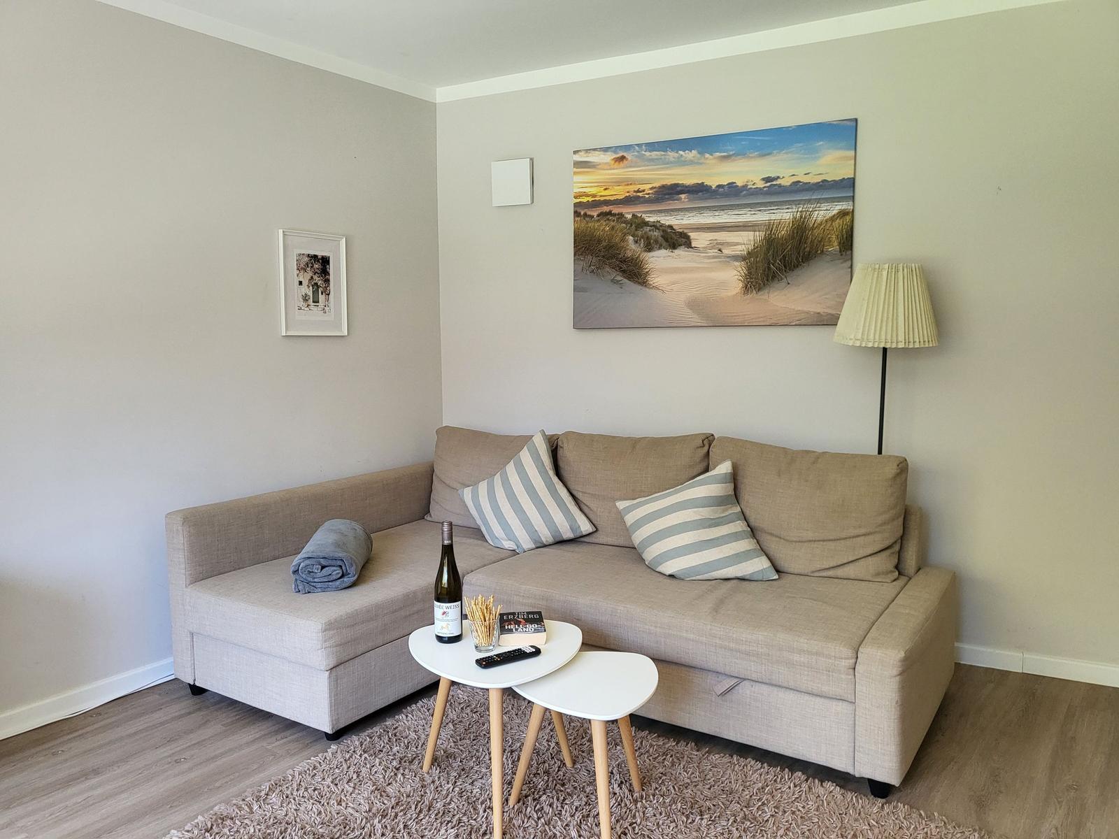 Ein Wohnzimmer mit Sofa, Tisch und Wandbild. Ein Flur führt weiter.