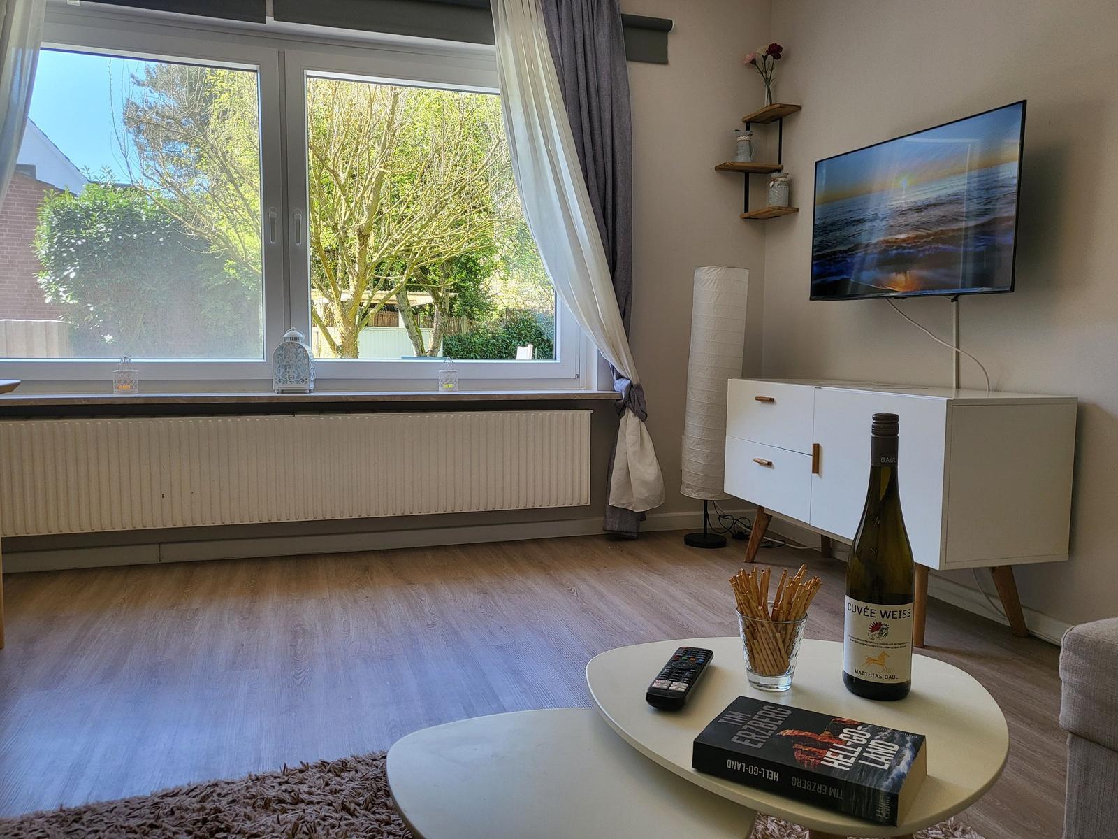 Wohnzimmer mit Fernseher, Tisch, Flur und Fensterblick auf Garten.
