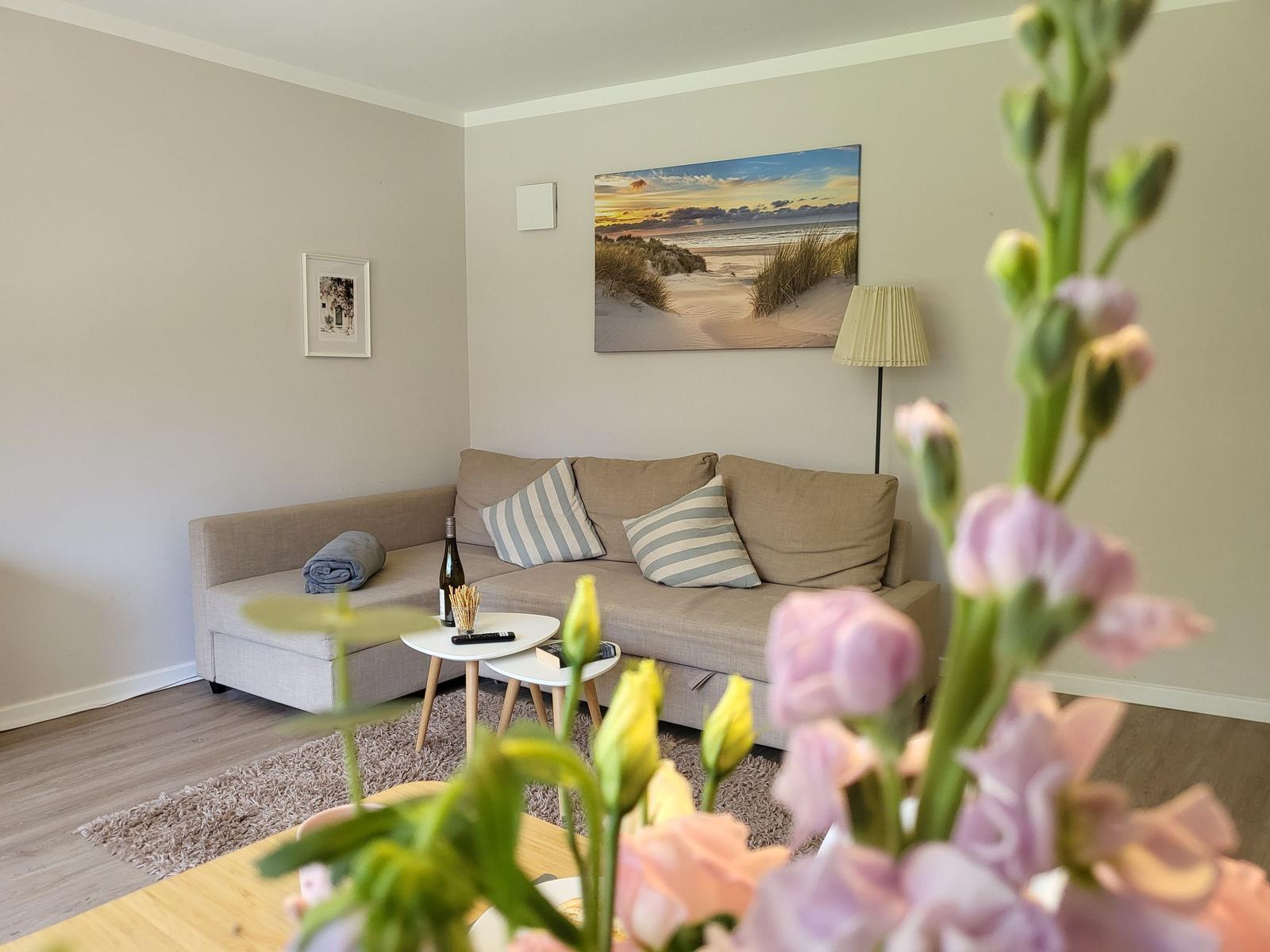 Wohnzimmer mit Sofa, Tisch und Wandbild. Blumen im Vordergrund.