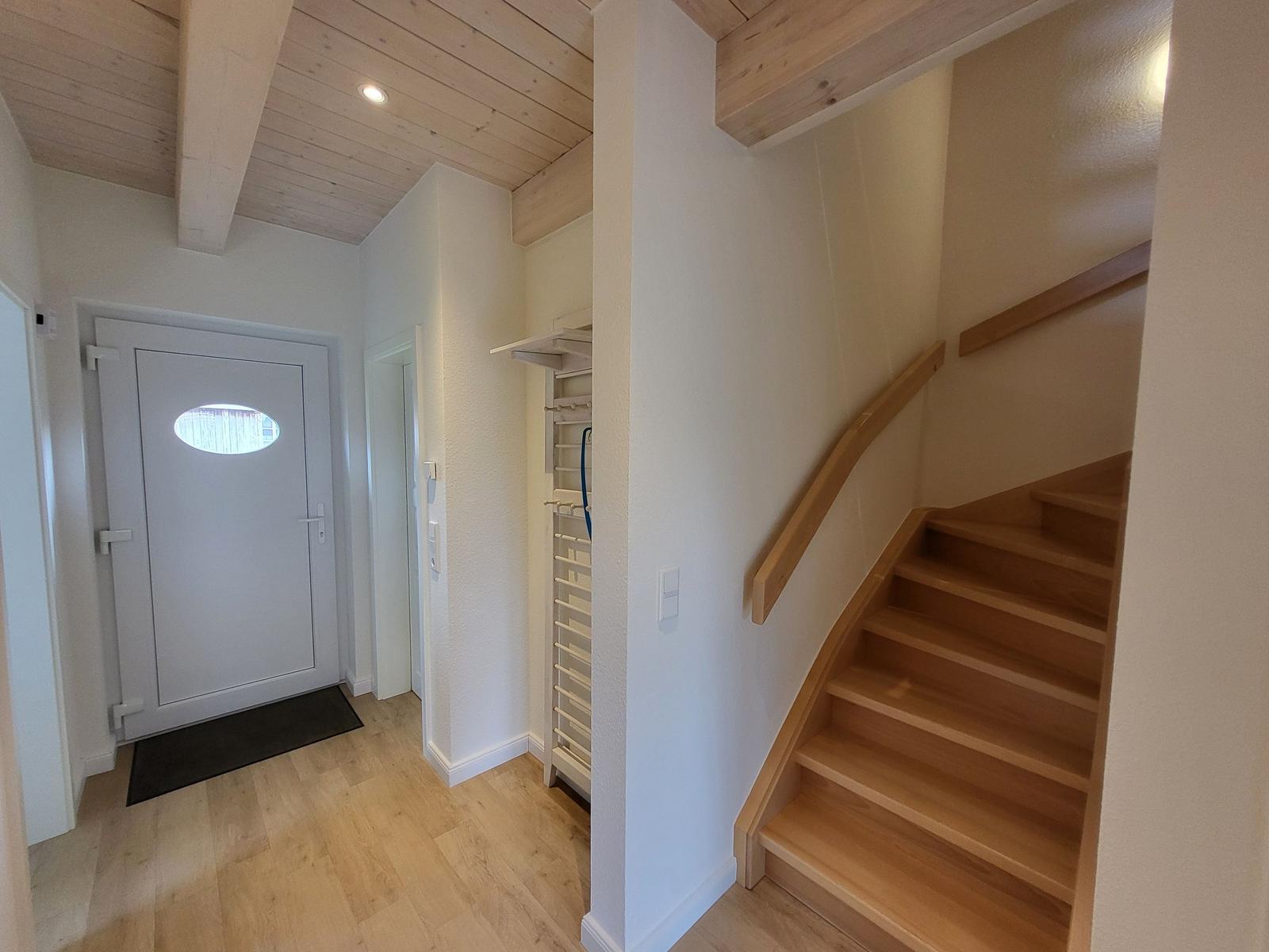 Eingang mit Holztreppe und weißen Wänden. Holzdecke und Tür mit runden Fenster.