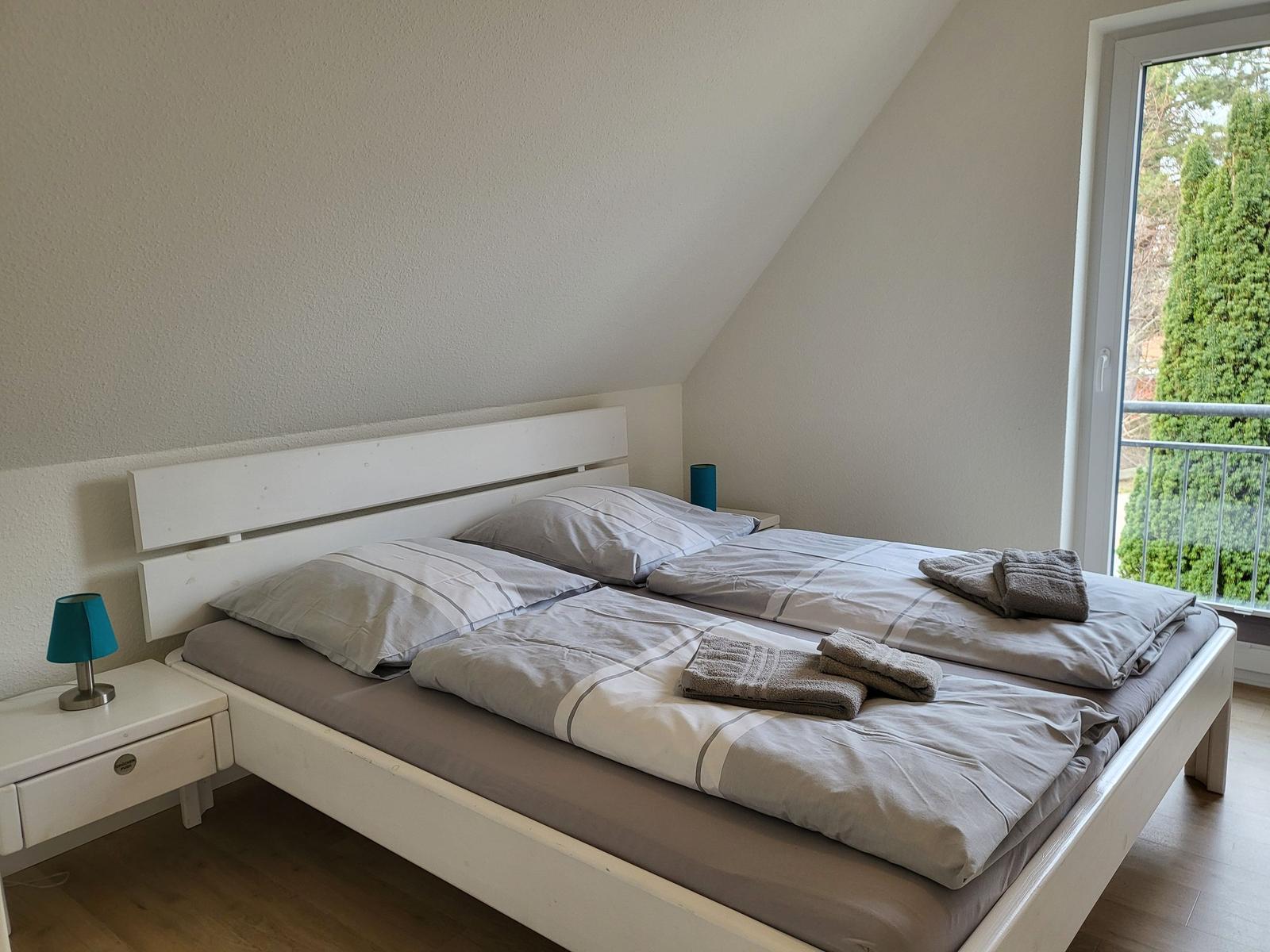 Schlafzimmer mit Doppelbett, Nachttisch und Balkonblick.