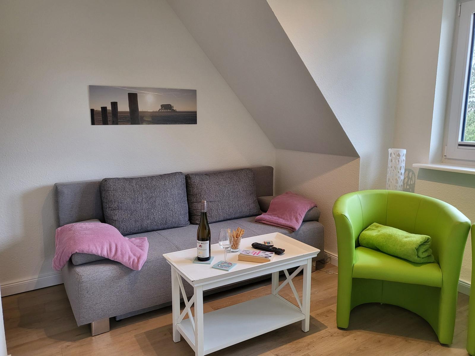 Wohnzimmer mit Sofa, grünem Sessel und Tisch unter schrägem Dach