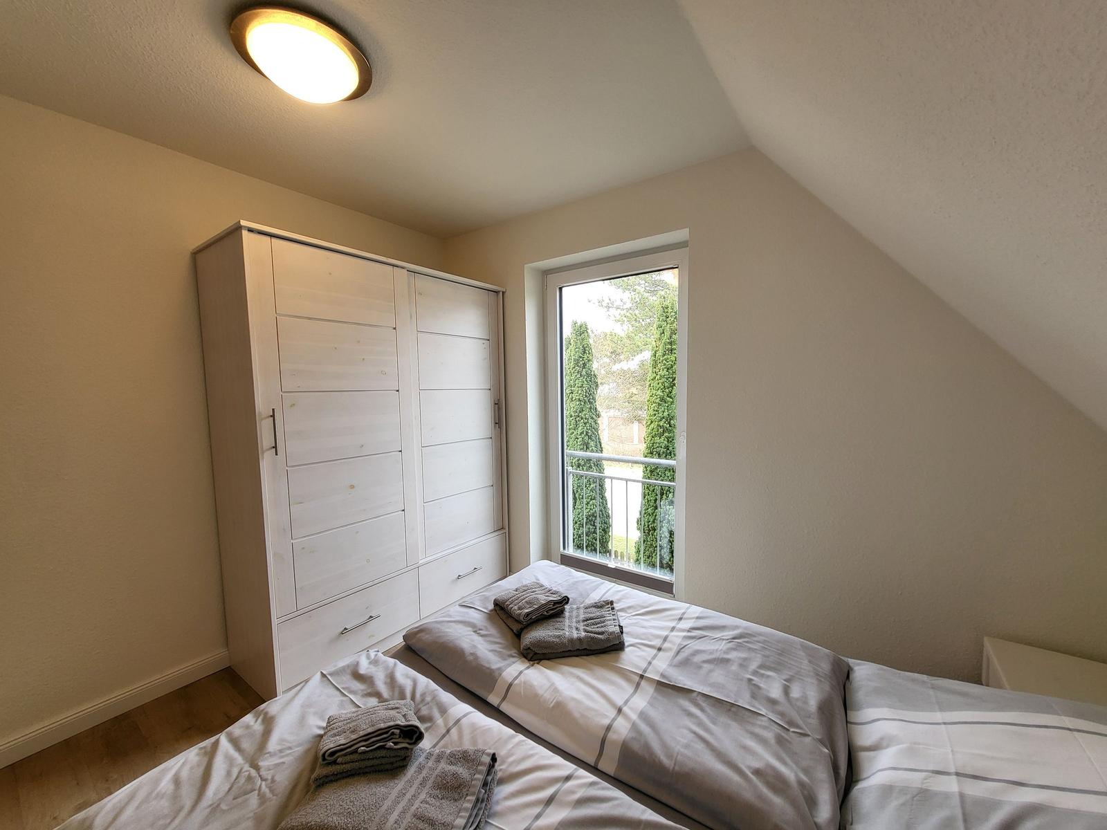 Schlafzimmer mit Doppelbett, Kleiderschrank und Fenster zum Balkon.
