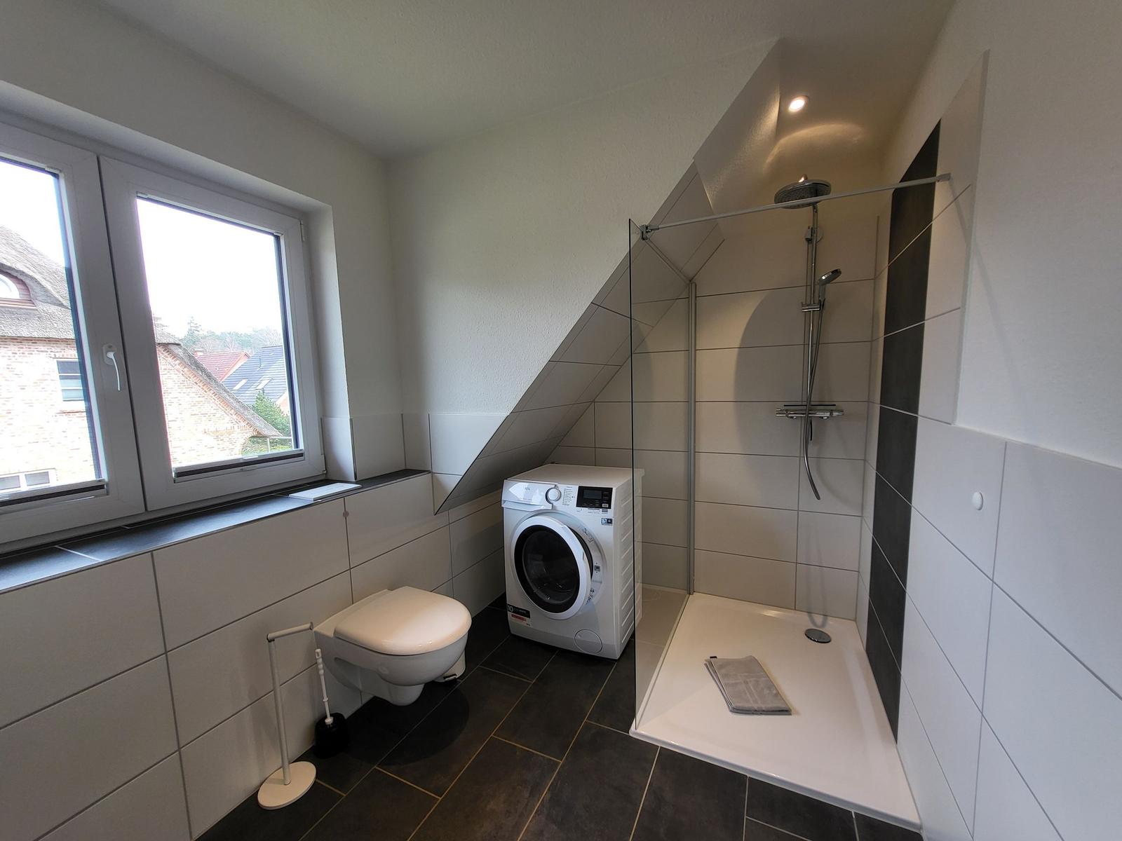Badezimmer mit Dusche, Waschmaschine und Fenster