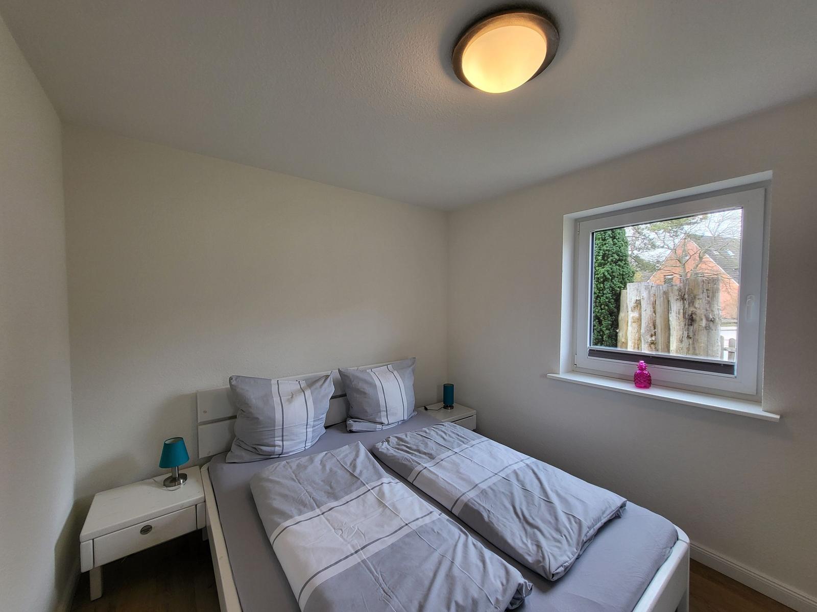 Schlafzimmer mit Doppelbett, Nachttisch und Fenster mit Blick nach außen.