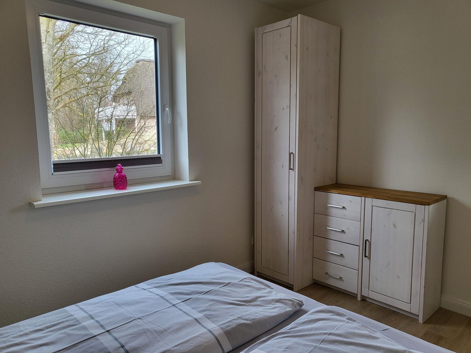 Schlafzimmer mit Bett, Kleiderschrank und Fenster mit Blick auf Außenbereich.