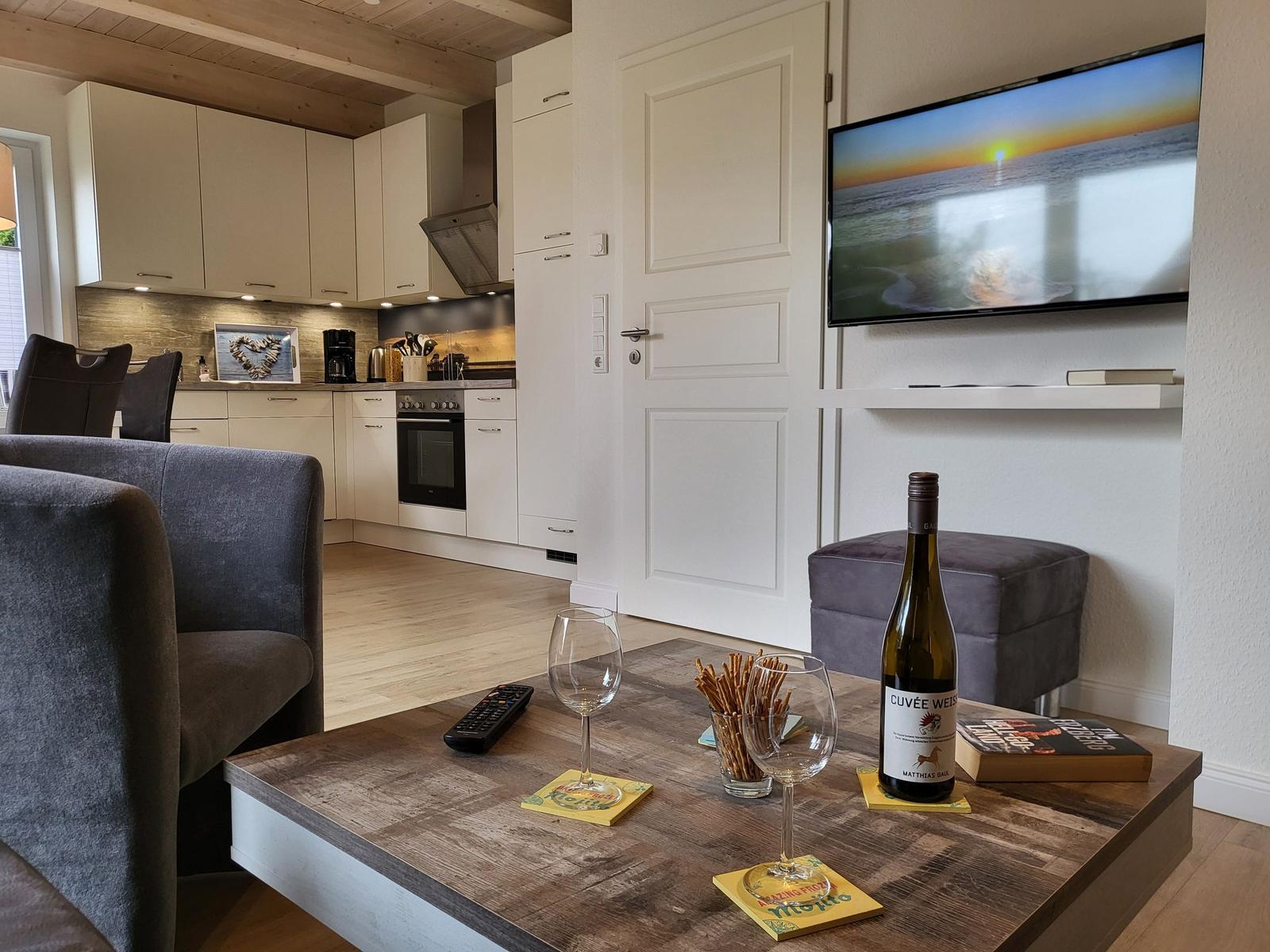 Wohn- und Küchenbereich mit Fernseher, Tisch mit Wein und Snacks.