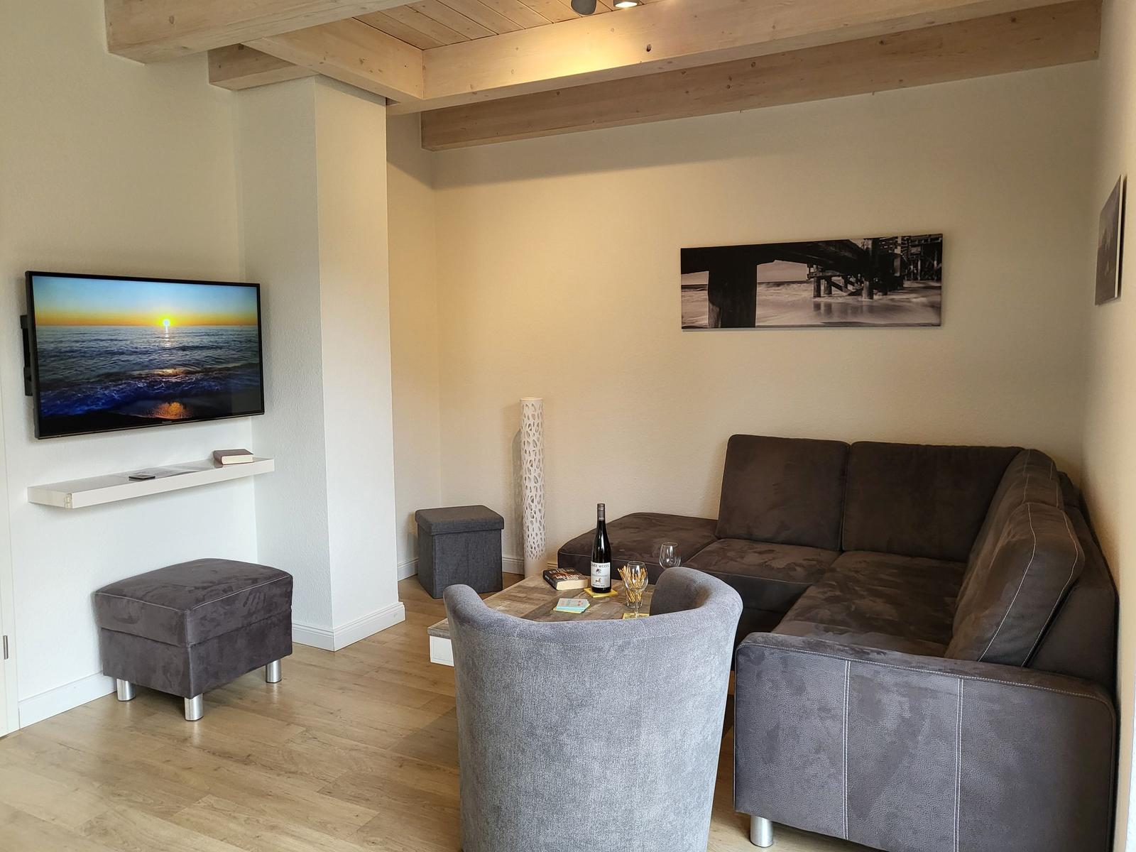 Wohnzimmer mit Sofa, Sessel und Fernseher an der Wand.