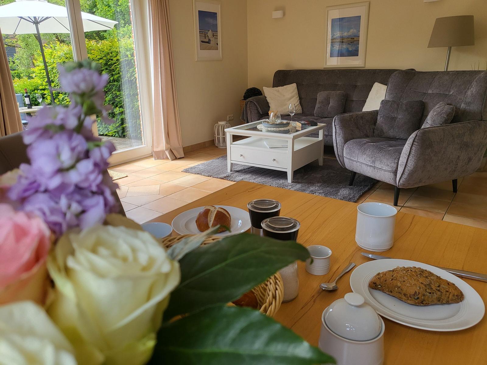 Wohnzimmer mit Sofa, Couchtisch und Blick auf Garten. Tisch mit Frühstück und Blumen.