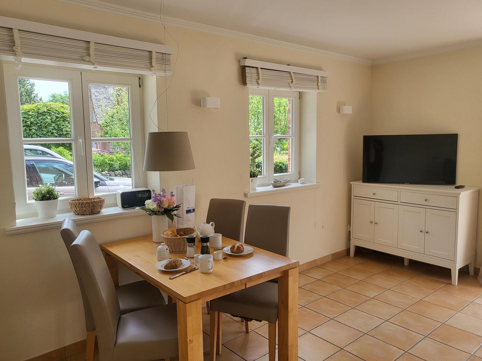 Esszimmer mit Tisch, Stühlen und TV. Fenster mit Blick auf Garten.