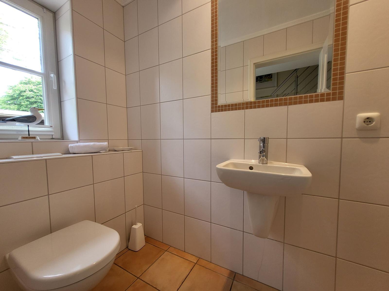 Badezimmer mit Waschbecken, Spiegel, Toilette und Fenster mit Vogeldekoration.