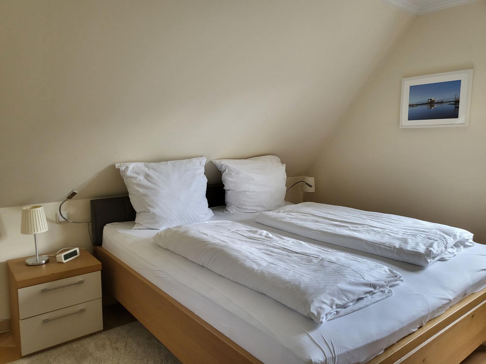 Schlafzimmer mit Doppelbett, Nachttisch und Wandbild.