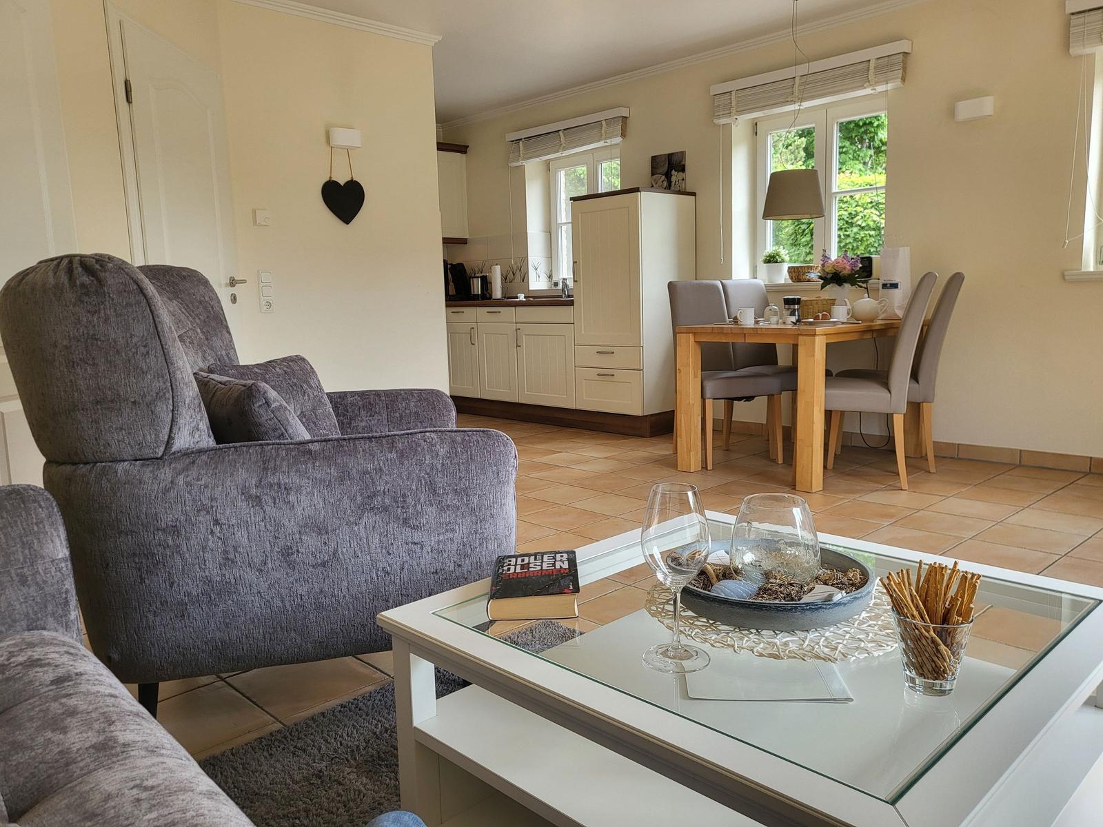 Wohnzimmer mit Sitzgruppe, Glas-Tisch und Blick in die Küche.