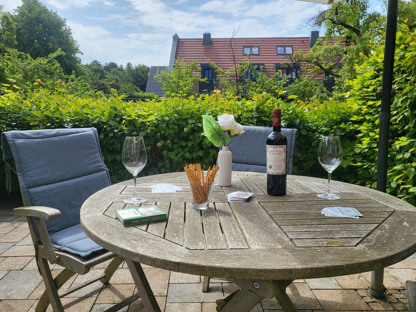 Runder Holztisch mit Stühlen, Wein und Snacks im Garten.