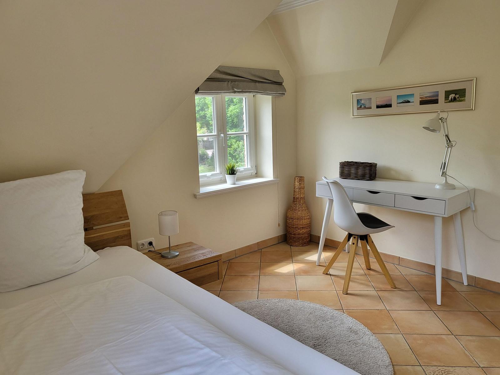 Schlafzimmer mit Bett, Schreibtisch und Fenster. Holzboden und Wandgestaltung.