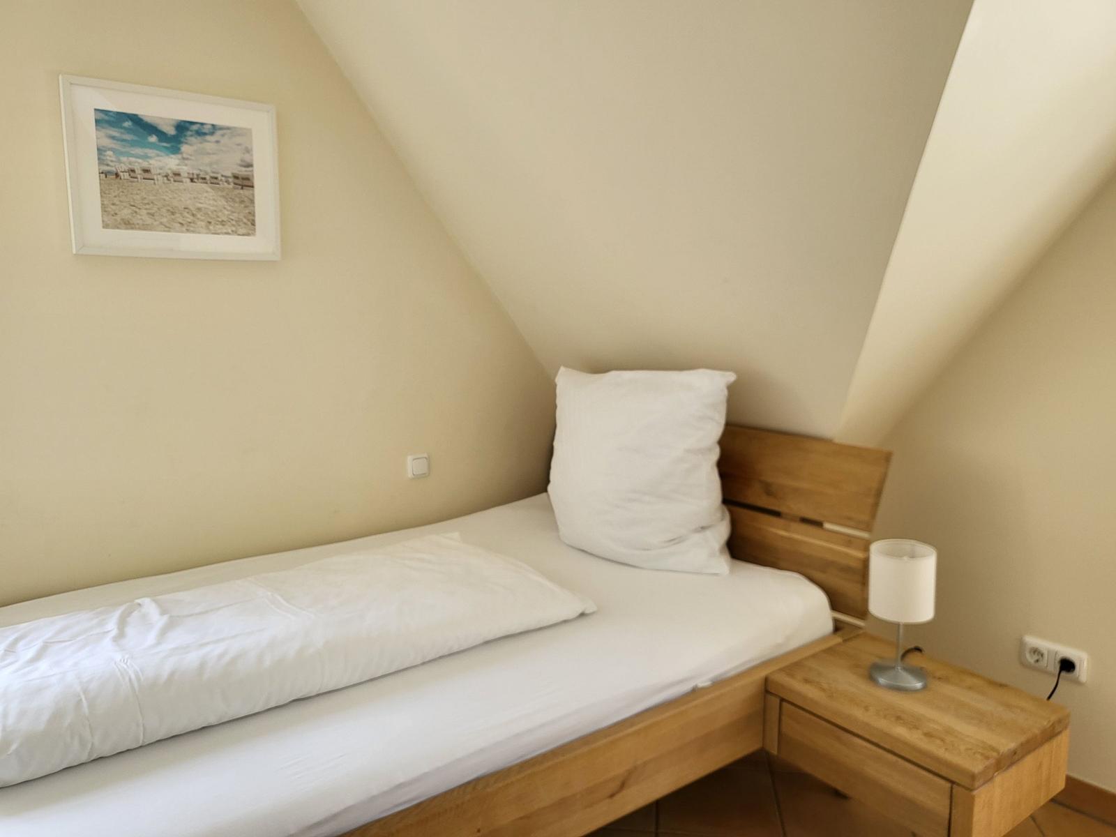 Schlafzimmer mit Dachschräge, Bett, Nachttisch und Wandbild.