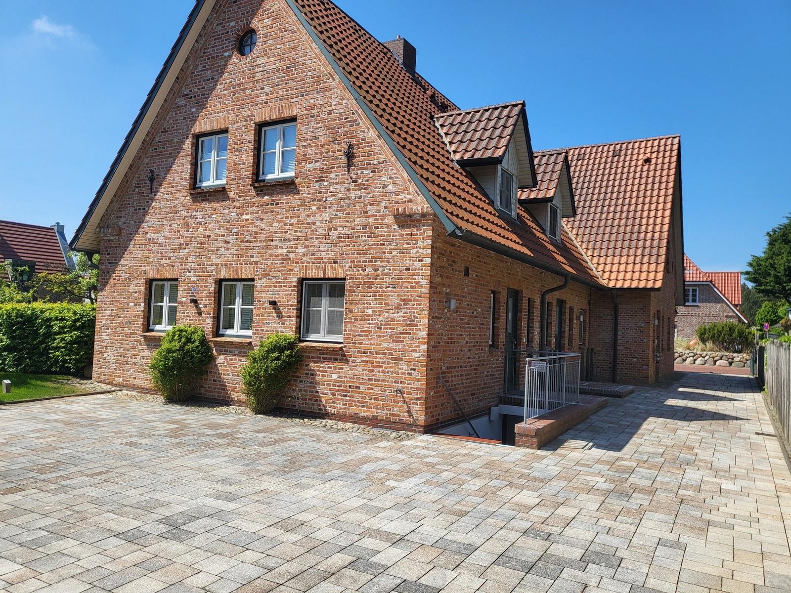 Ein zweistöckiges Backsteingebäude mit rotem Ziegeldach und gepflastertem Vorplatz.