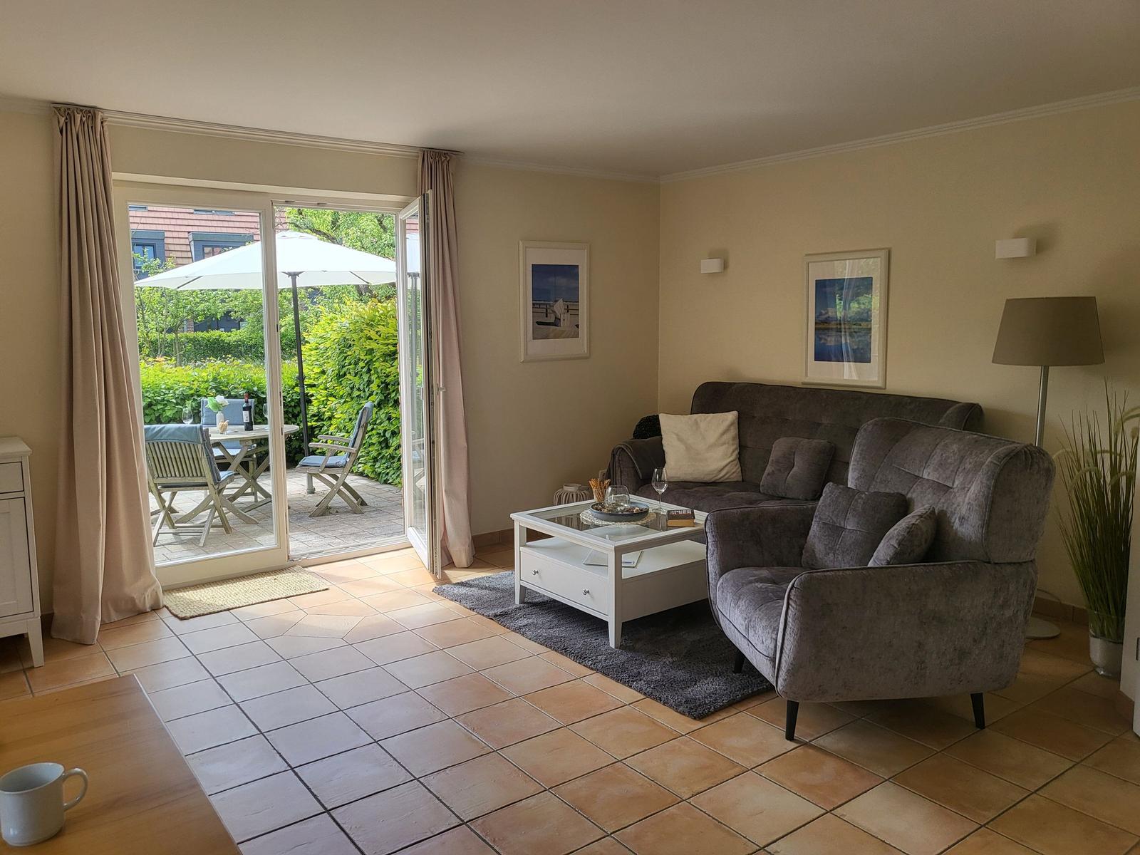 Wohnzimmer mit grauem Sofa, weißem Couchtisch und Terrasse mit Tisch und Stühlen.