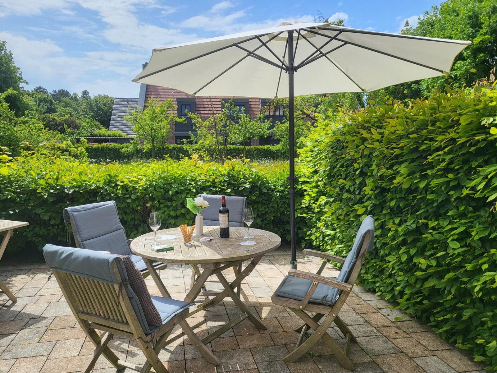 Terrasse mit Tisch, Stühlen und Sonnenschirm. Hinterhof mit grünen Hecken.