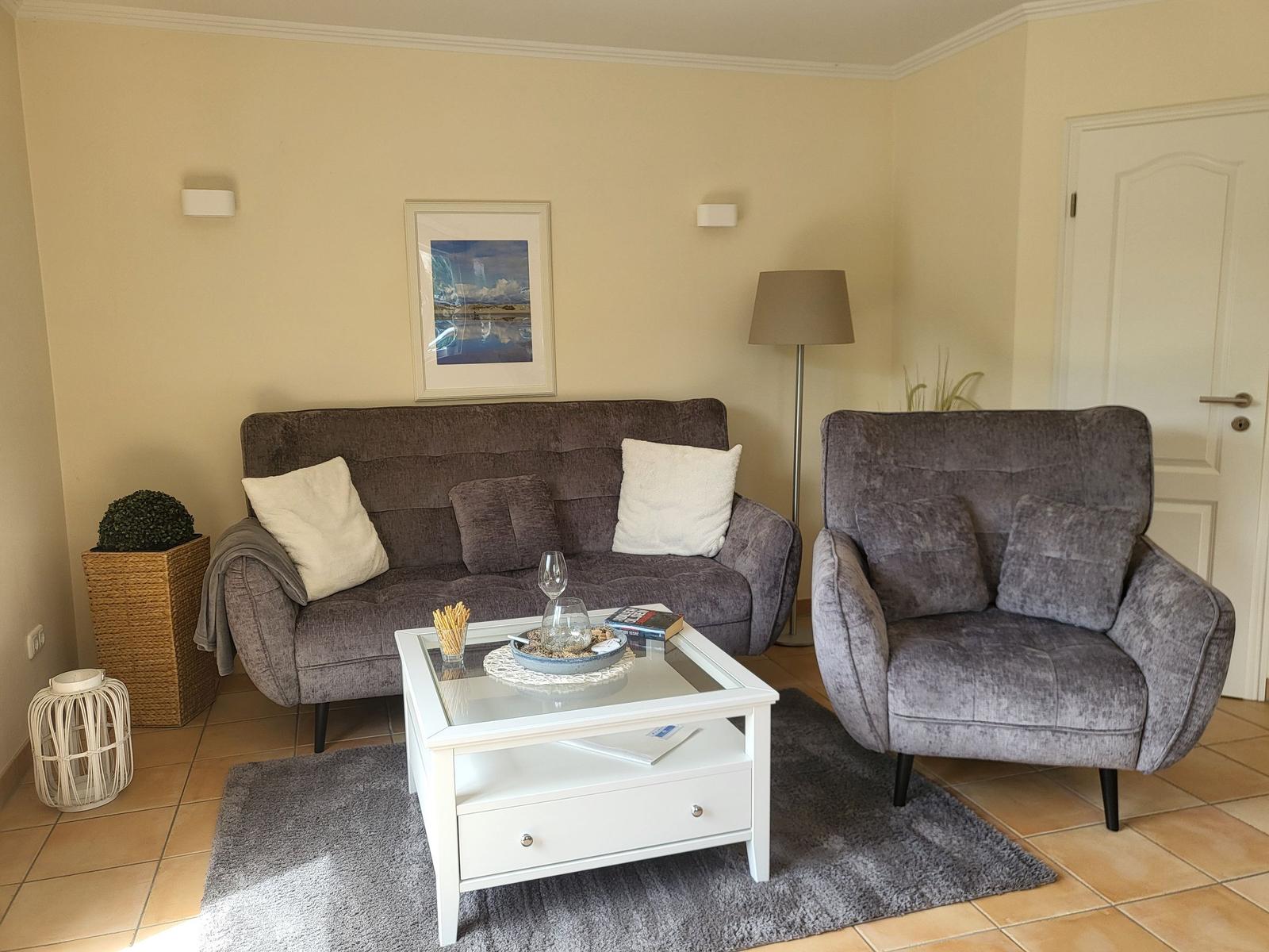 Wohnzimmer mit grauem Sofa, Sessel, Glas-Tisch und Teppich