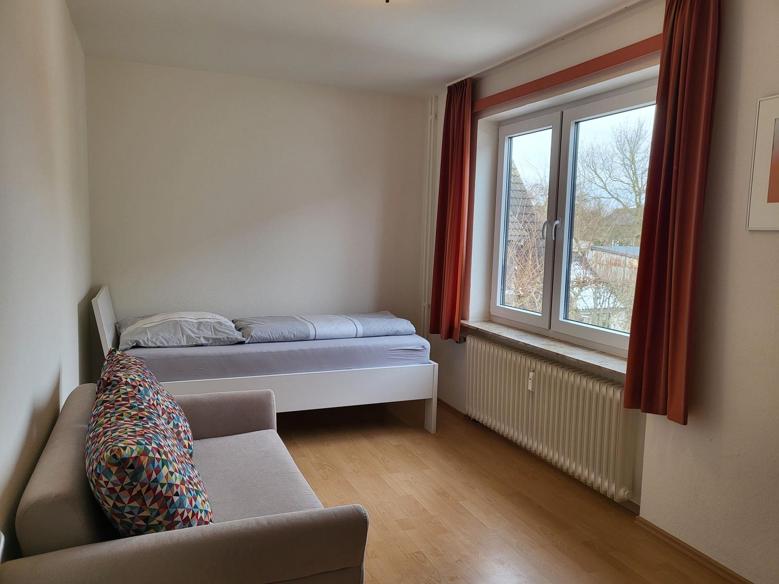 Zimmer mit Bett, Sofa und Fenster mit Blick nach draußen.