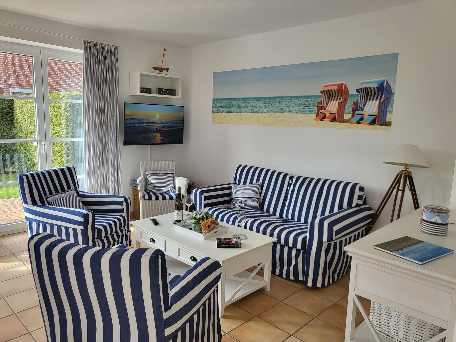 Wohnzimmer mit Streifenmöbeln, Fernseher und Strandbild an der Wand.