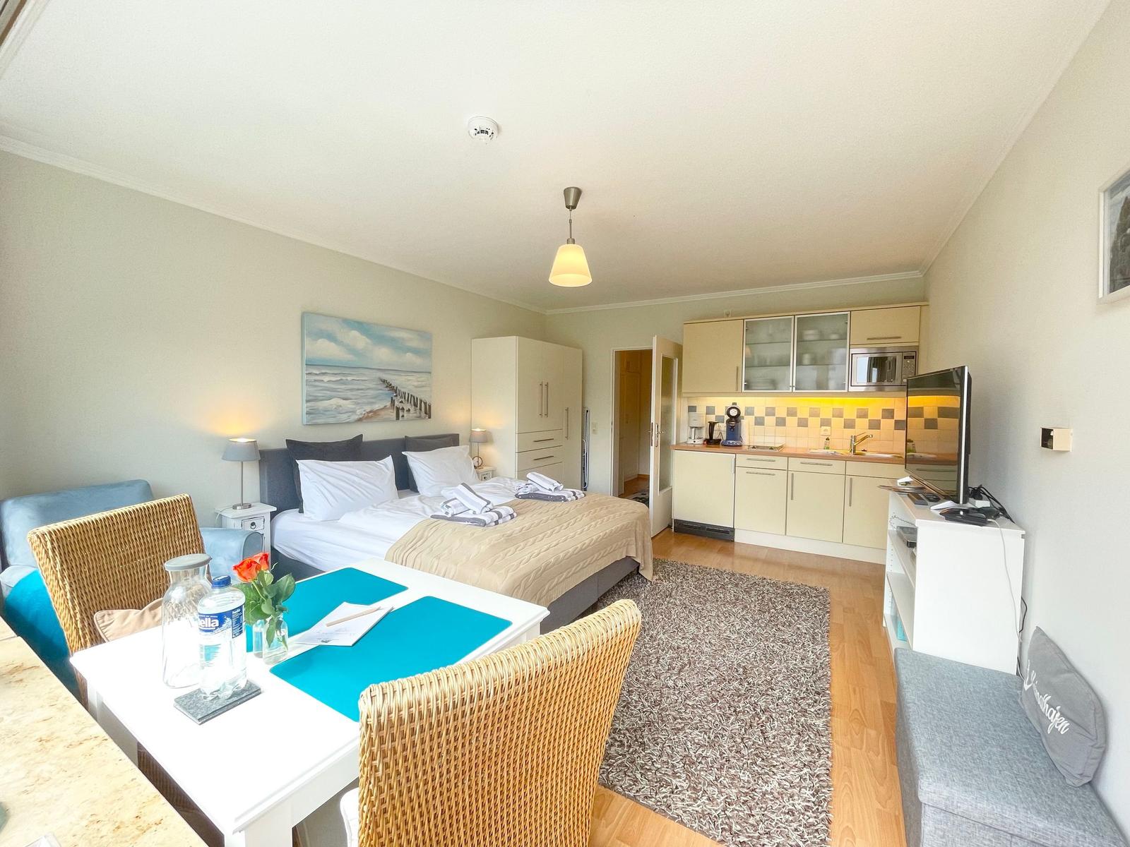 Schlafzimmer mit Bett, Essplatz und Küche. Wandbild zeigt Strand.