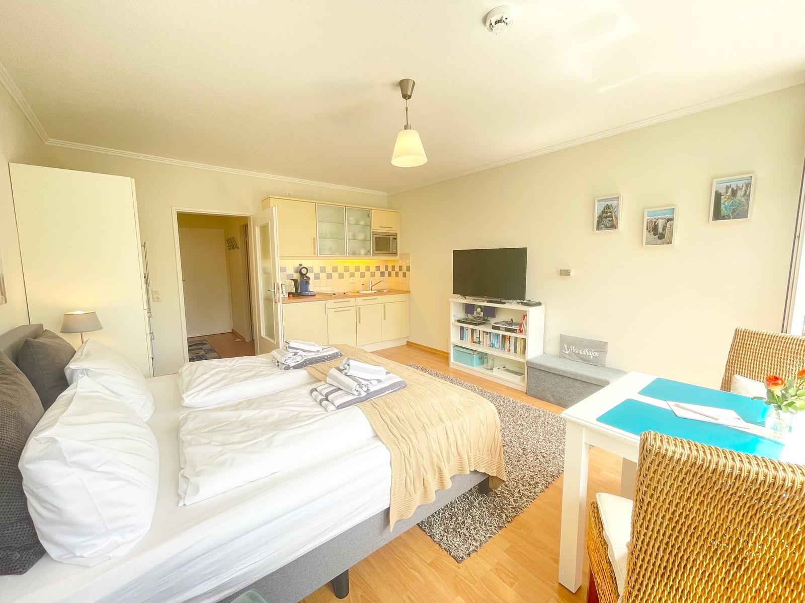 Schlafzimmer mit Bett, Küchenzeile, TV und Esstisch mit Stühlen.