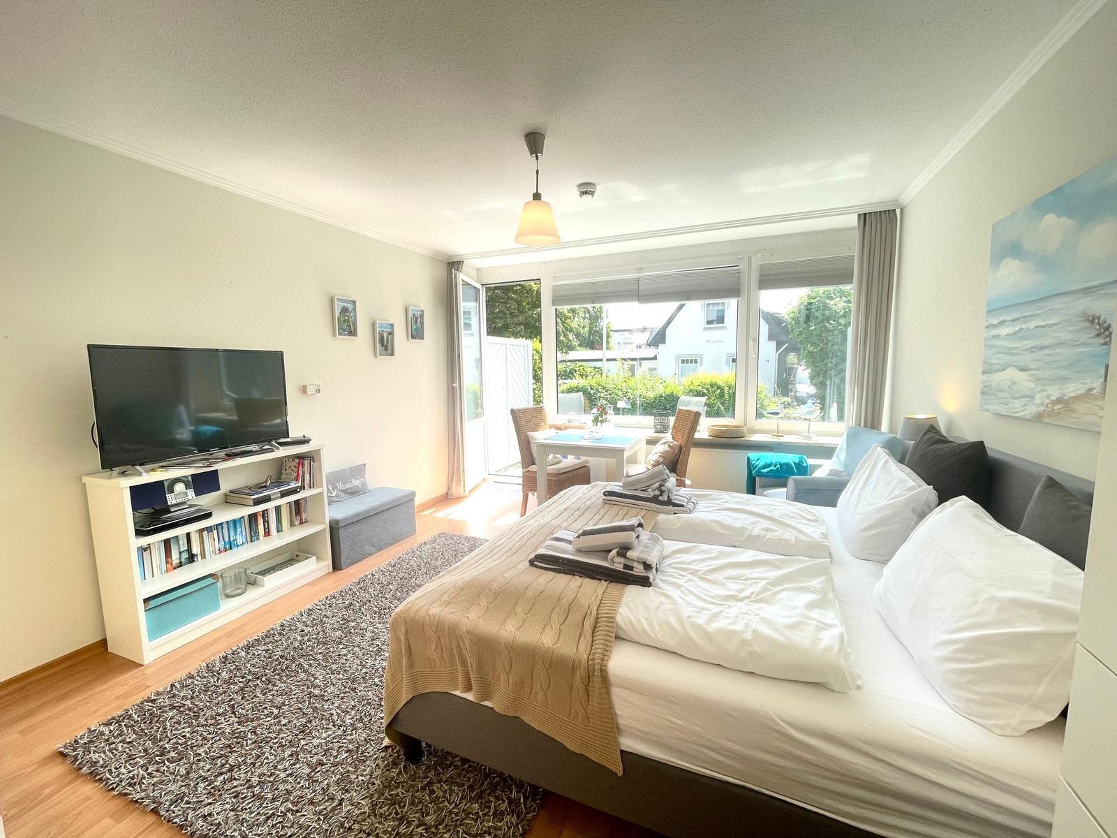 Schlafzimmer mit Doppelbett, Fernseher und Blick auf Balkon.