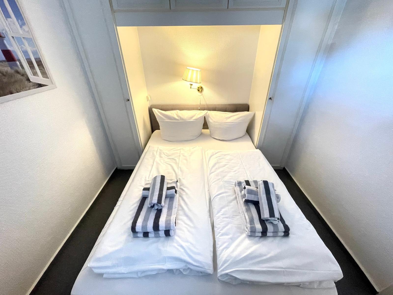 Zimmer mit Doppelbett, zwei Kissen und gefalteten Handtüchern.