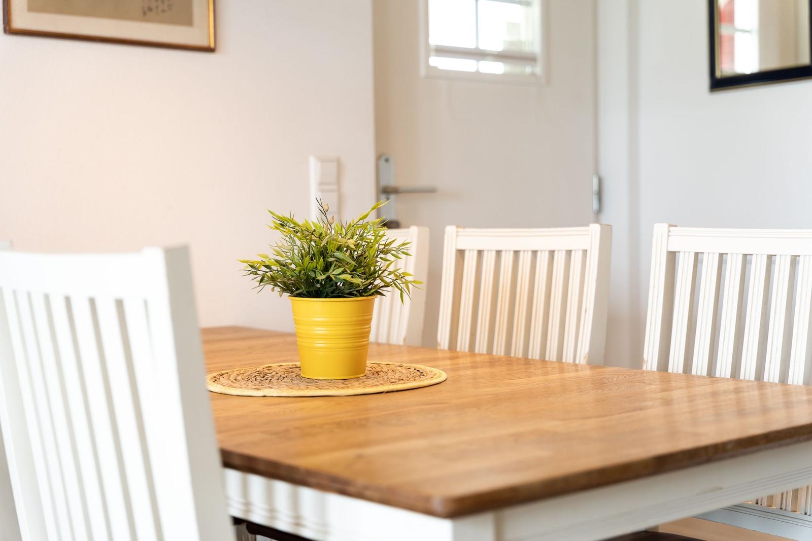 Dining table with four white chairs and yellow plant on round mat.
