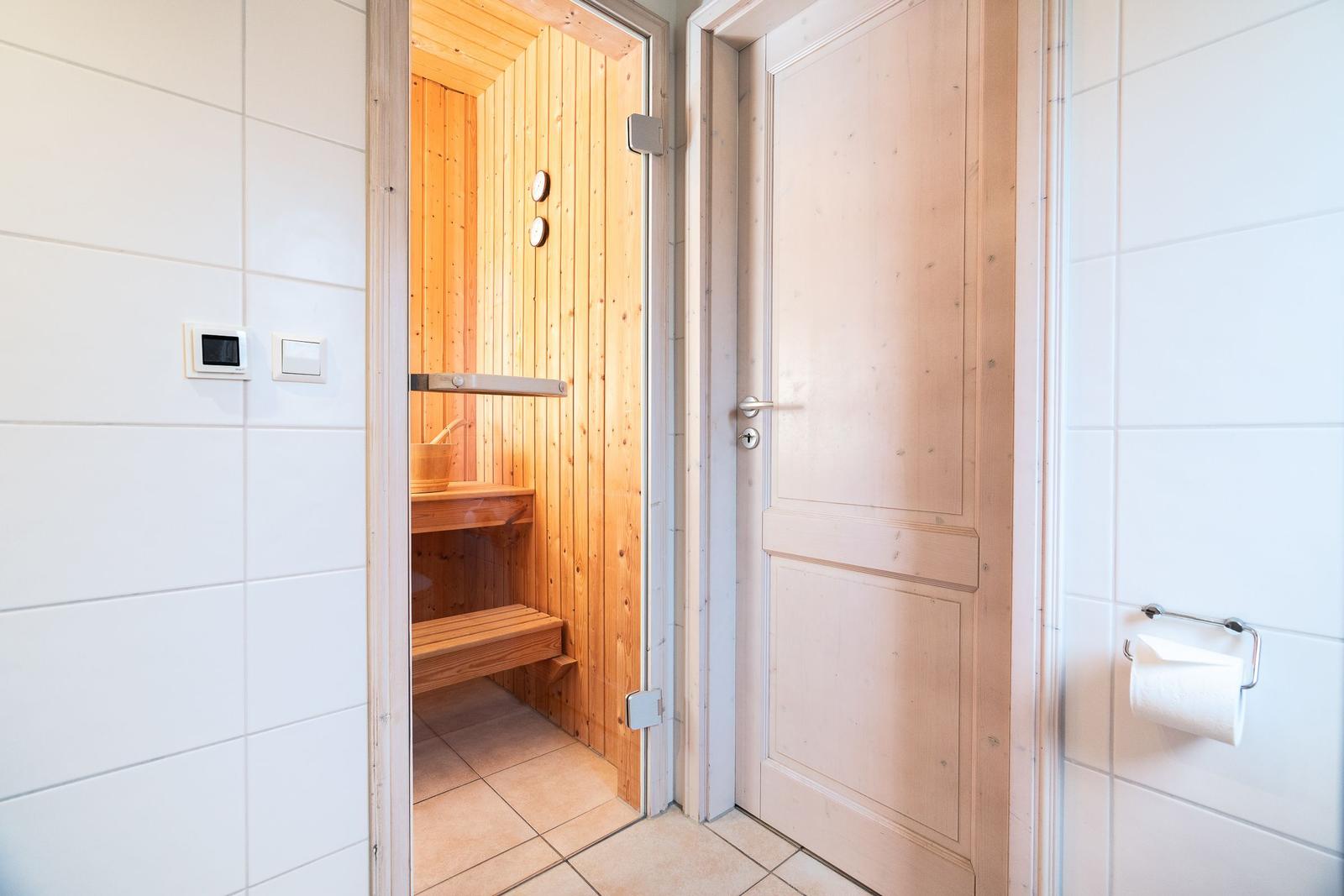 Sauna with wooden cladding and bench. Door and toilet paper holder are visible.