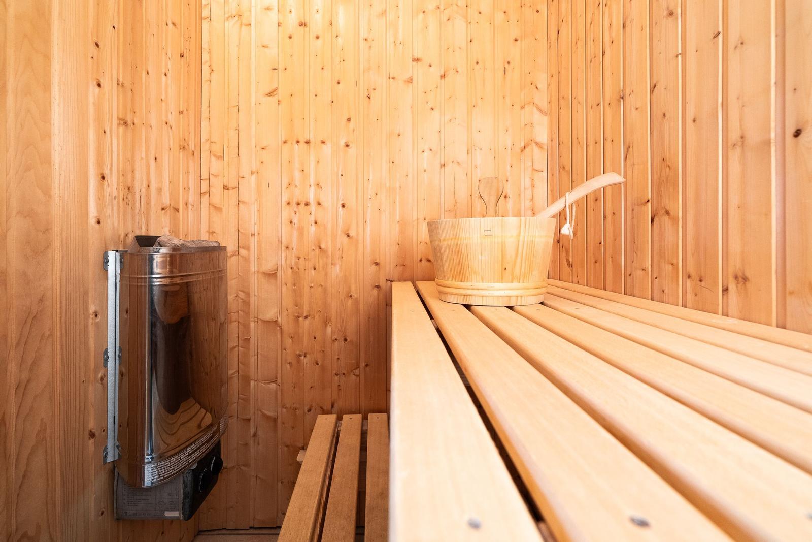 Sauna with wooden bench, wooden bucket, and heater on the wall.