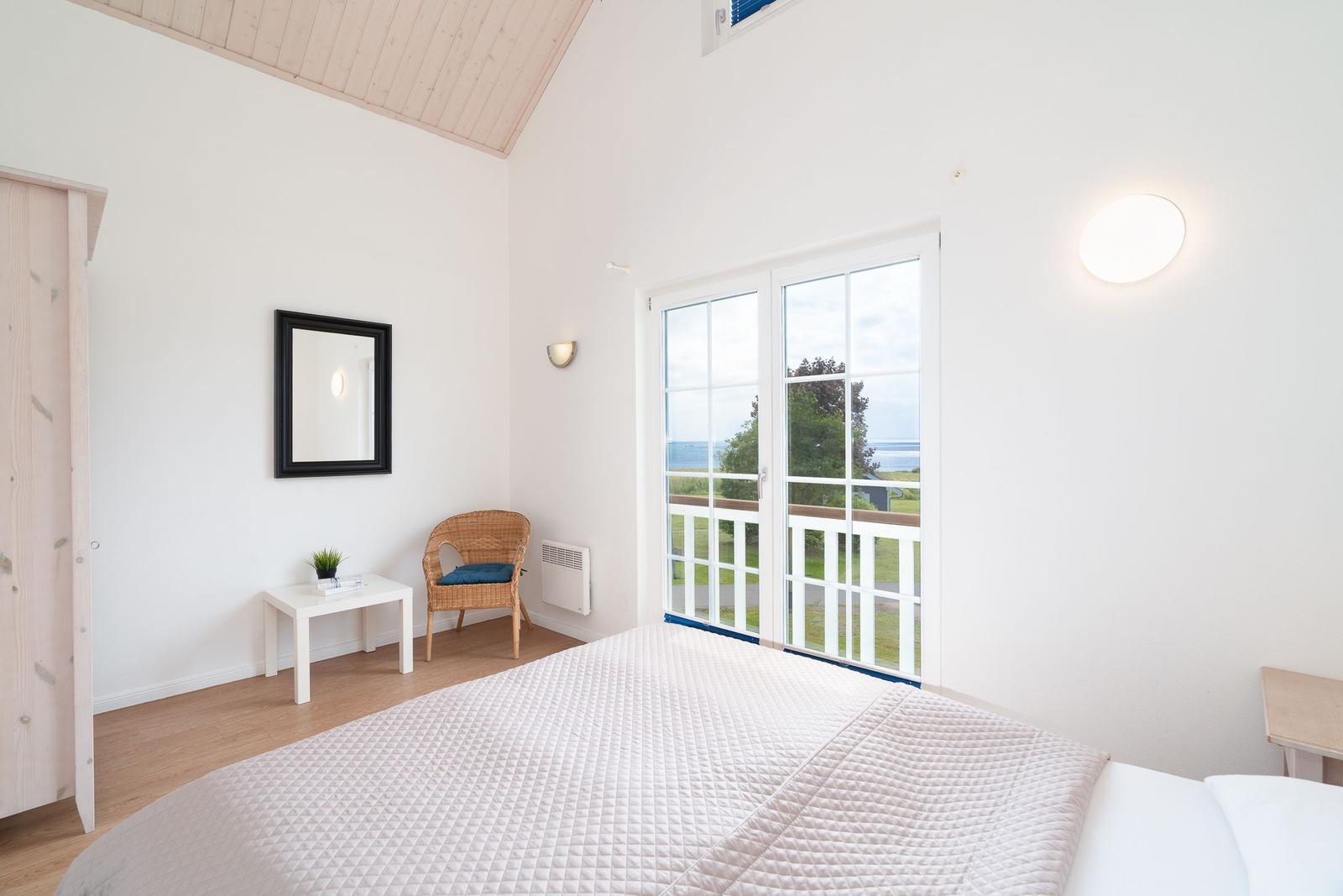 Bedroom with view of the lake, white walls, wooden floor, and balcony door.