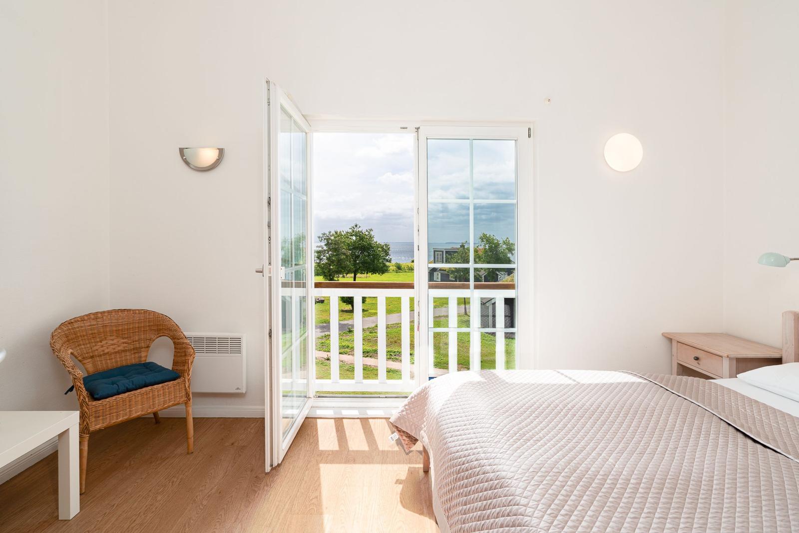 Bedroom with balcony, bed, chair, and view of green area.
