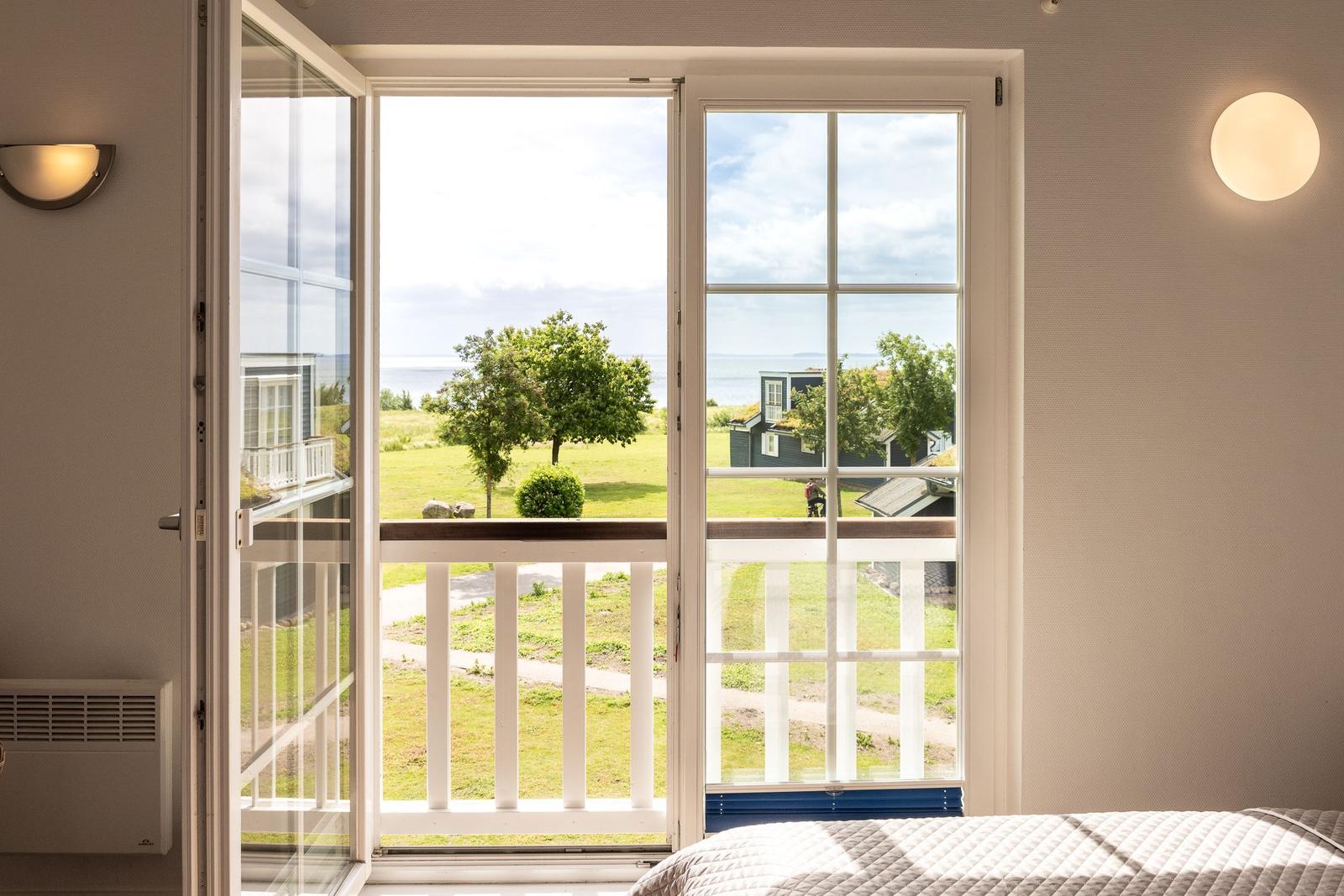 Through the glass door, you can see a balcony with a view of grass and sea.