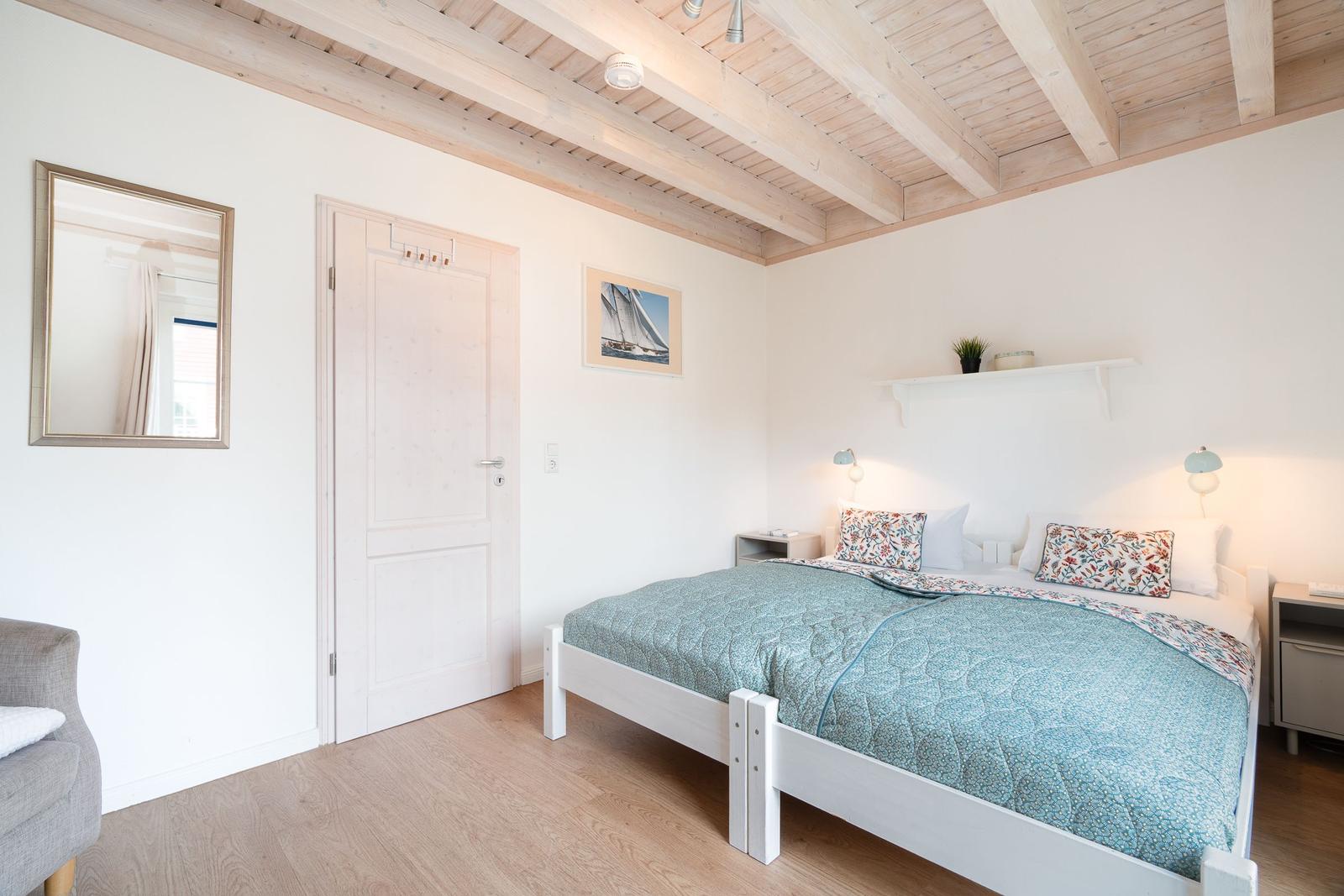 Bedroom with white bed, wooden ceiling, and mirror on the wall.