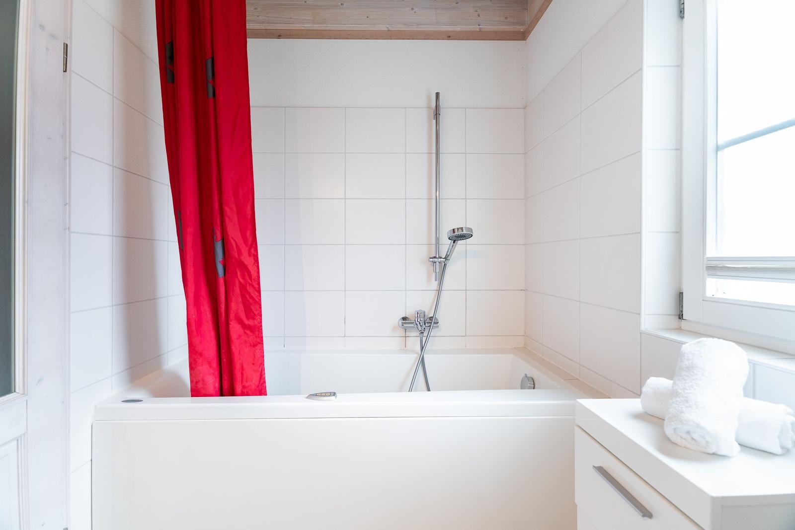 Bath with bathtub, red shower curtain, and window with towels.