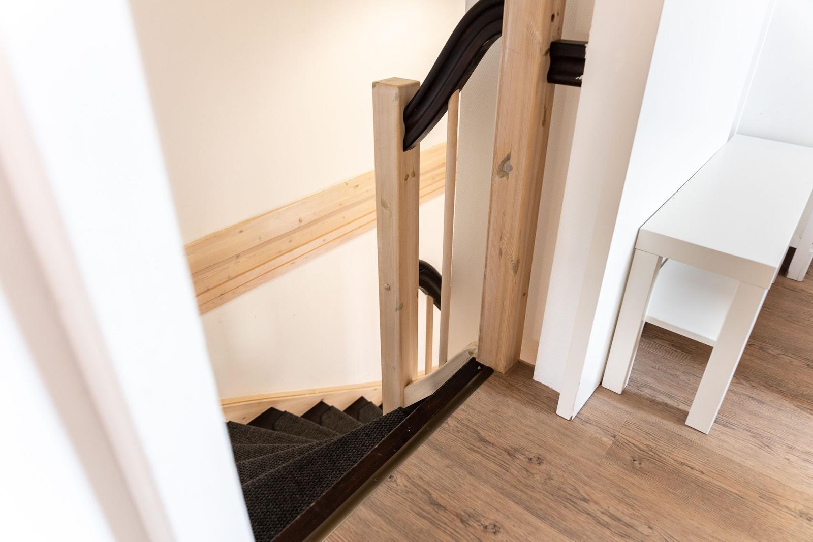 Staircase with wooden railing and black handrail. White bench beside the stairway.