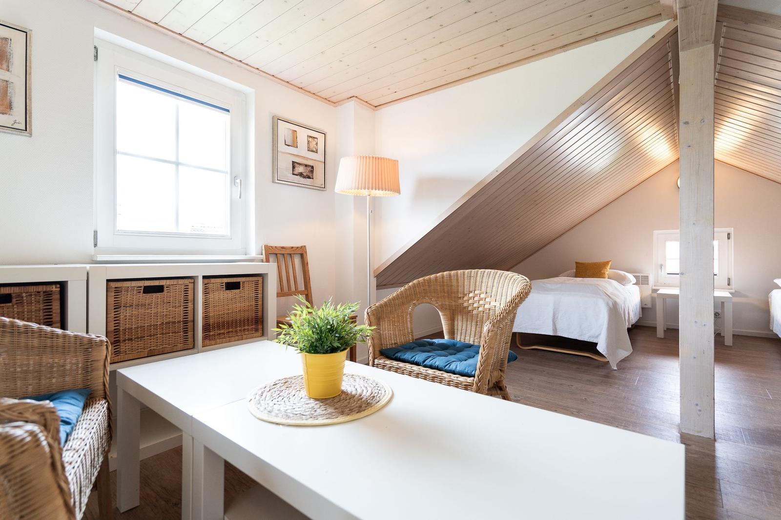 A bedroom with a sloped ceiling, bed, wicker chairs, and window.