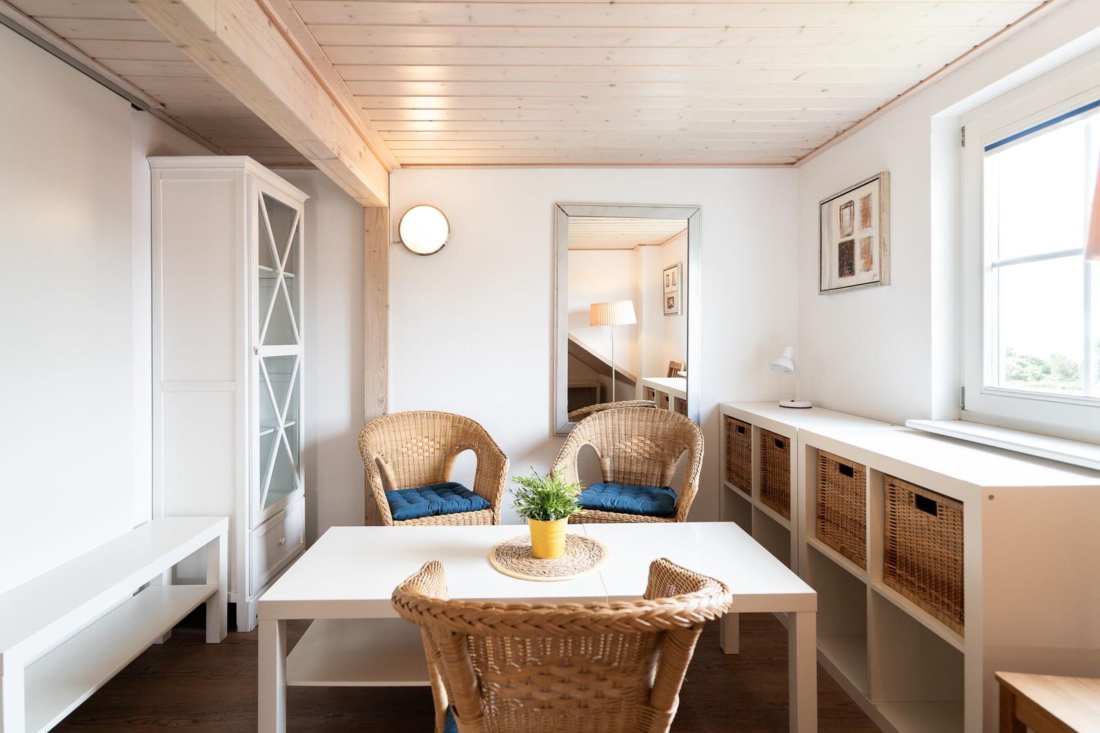 Dining area with white table, three wicker chairs and blue cushions. Window, shelves and cabinet are visible.
